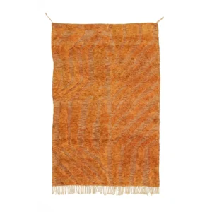 A luxurious, large orange rug with abstract zigzag patterns and fringe at the bottom edge hangs against a plain white background, showcasing exquisite craftsmanship in handmade home decor.