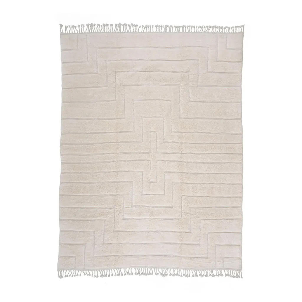 A luxurious beige rug, hand-knotted with an intricate geometric pattern and fringes on the shorter edges, adds an elegant touch to any space.