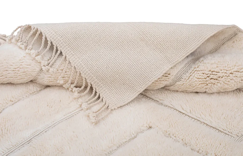A beige textured piece with fringe is elegantly draped, exuding the refined beauty often found in hand-knotted rugs.