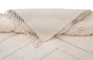A beige textured piece with fringe is elegantly draped, exuding the refined beauty often found in hand-knotted rugs.