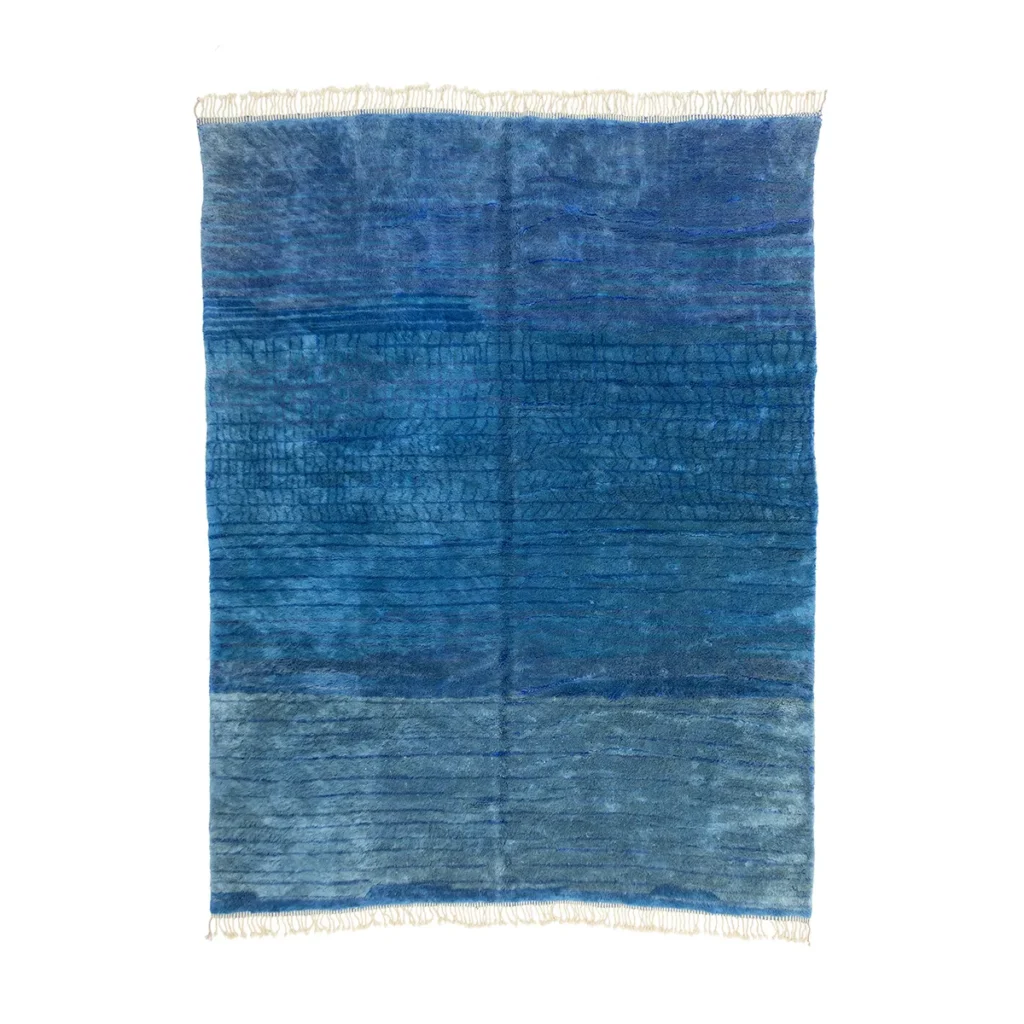 This artisanal rug showcases a blue textured design with fringed edges, featuring hand-knotted horizontal stripes and subtle variations in shade from dark to light blue.