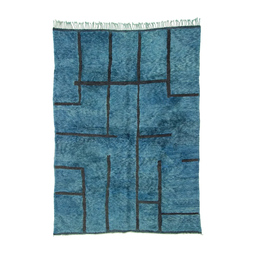 This hand-knotted blue rug features black geometric lines forming rectangular patterns. With fringed edges at the top and bottom, it embodies the qualities of authentic Moroccan rugs, adding a touch of artisanal elegance to any space.