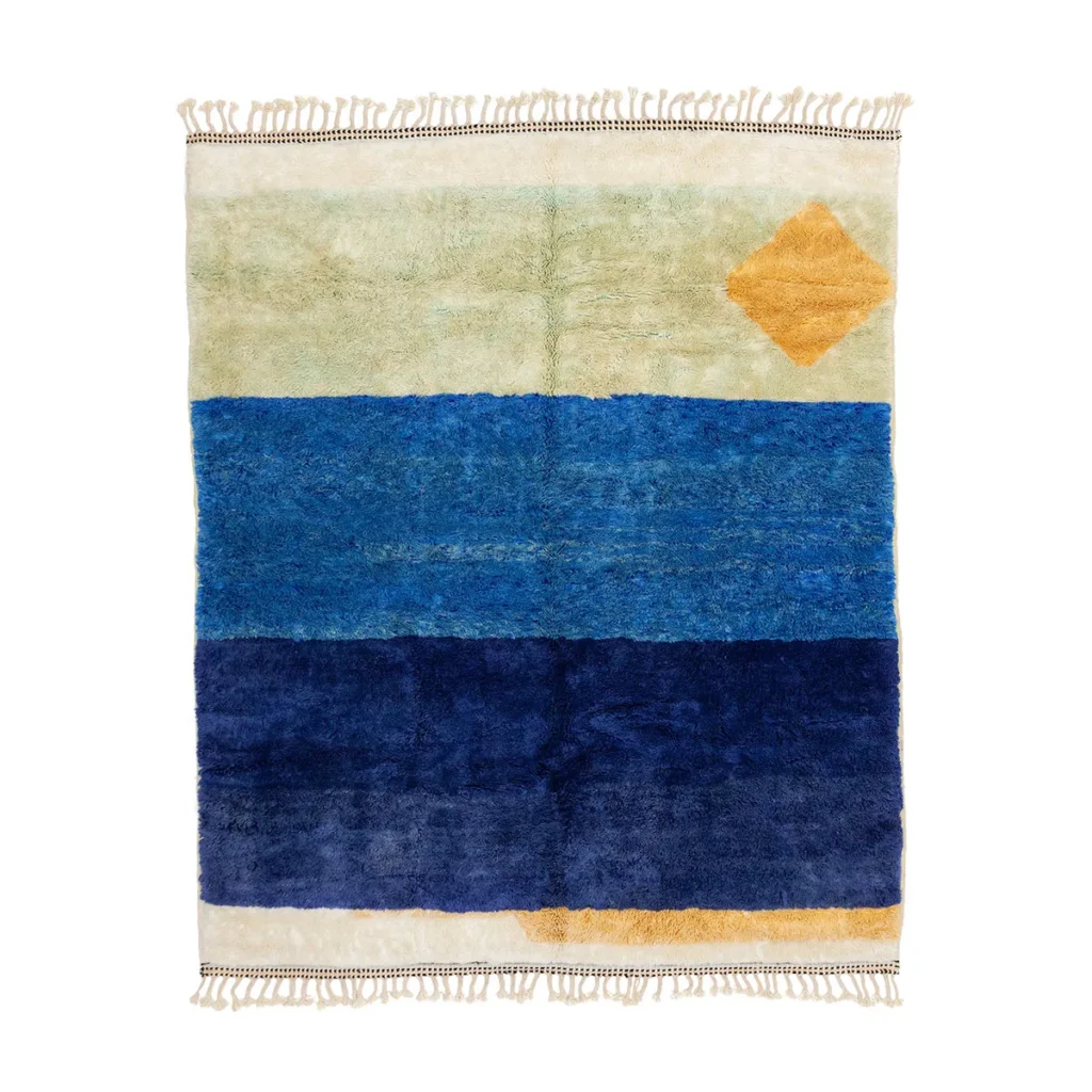 This artisanal rug features horizontal bands of green, light blue, and navy blue. A yellow diamond shape accents the upper right corner. Hand-knotted fringes elegantly adorn the top and bottom edges, reflecting its meticulous craftsmanship.