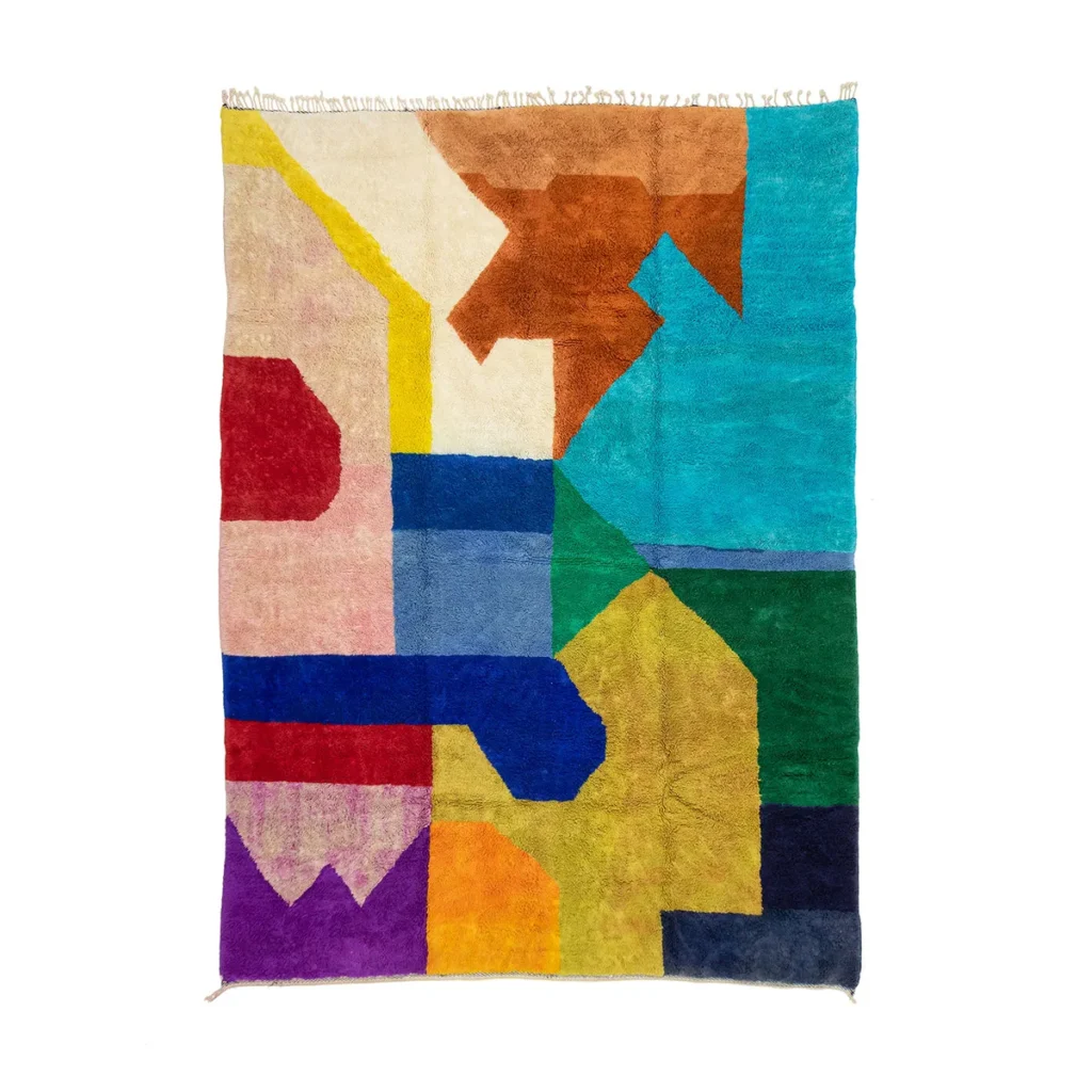 A vibrant, abstract geometric rug featuring an artisanal blend of shapes and blocks in rich shades of red, blue, yellow, green, and brown against a white background. This hand-knotted piece adds a touch of artistry to any space.