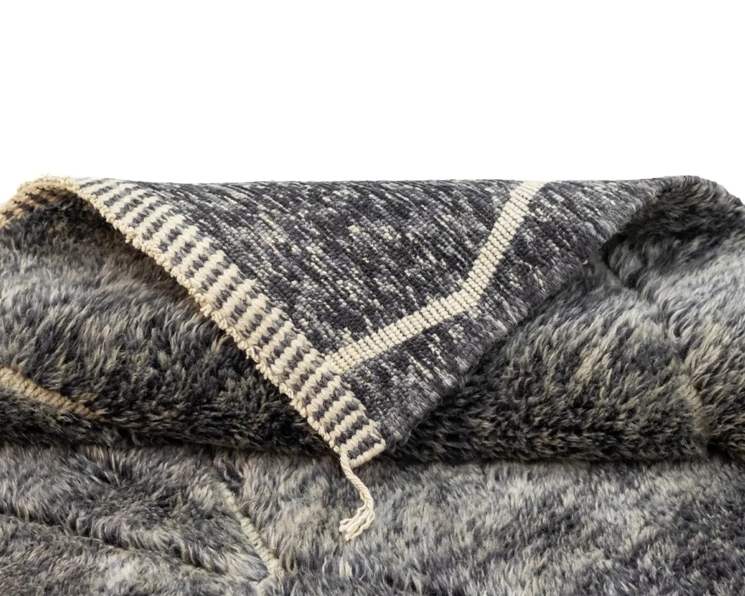 A cozy, hand-knotted faux fur piece in gray and black features a woven beige and gray pattern along the edge, set against a plain white background.