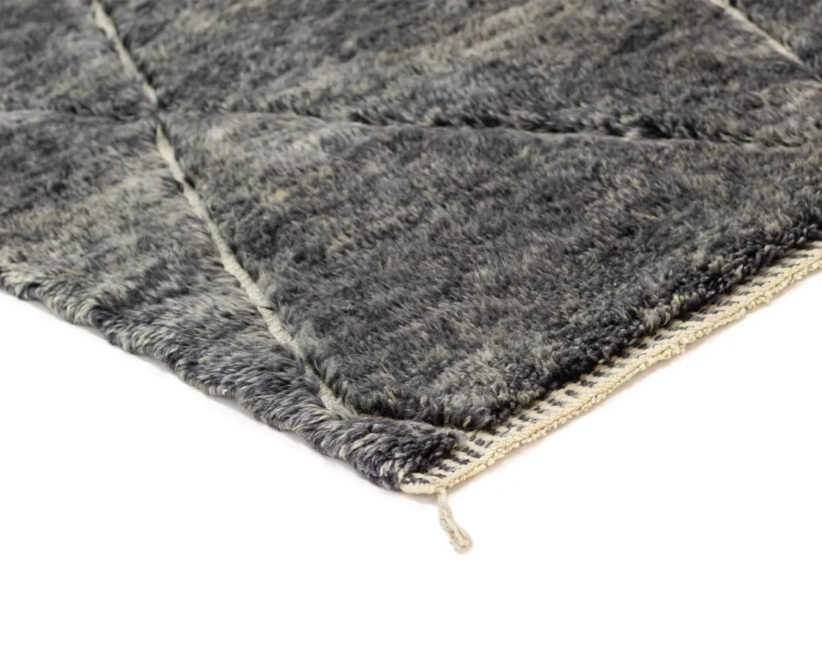 Close-up of a corner of a gray, textured, hand-knotted rug with a beige border and a loose thread hanging.