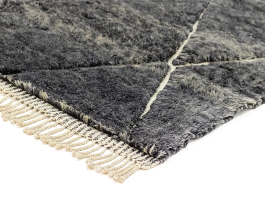 Close-up of a corner of a gray shaggy, hand-knotted rug with a geometric pattern and fringed edges, showcasing the artisanal craftsmanship.