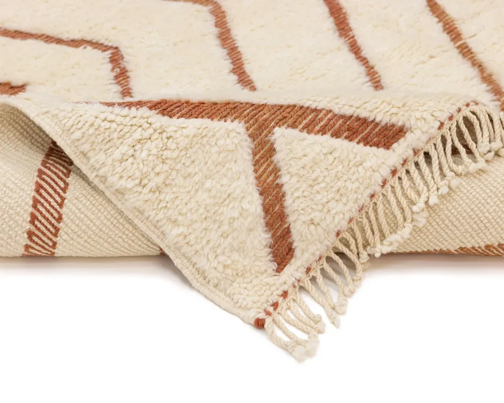 A luxurious hand-knotted rug in beige and brown, showcasing an intricate pattern with fringed edges and exquisite texture detail.