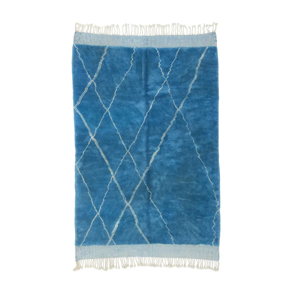 This artisanal rug features a blue hue with a diamond pattern and fringed edges, embodying the craftsmanship of authentic Moroccan rugs.