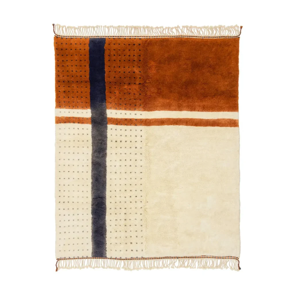 An artisanal rug with a geometric design showcases rust, cream, and navy hues, complemented by fringed edges.