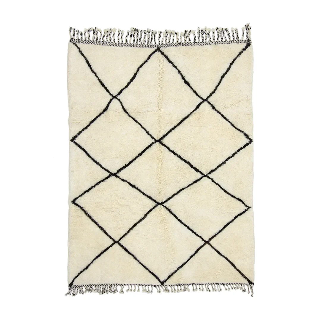 This luxurious cream-colored rug features a striking black diamond pattern and elegant fringed edges on the shorter sides, embodying the timeless craftsmanship of hand-knotted rugs.