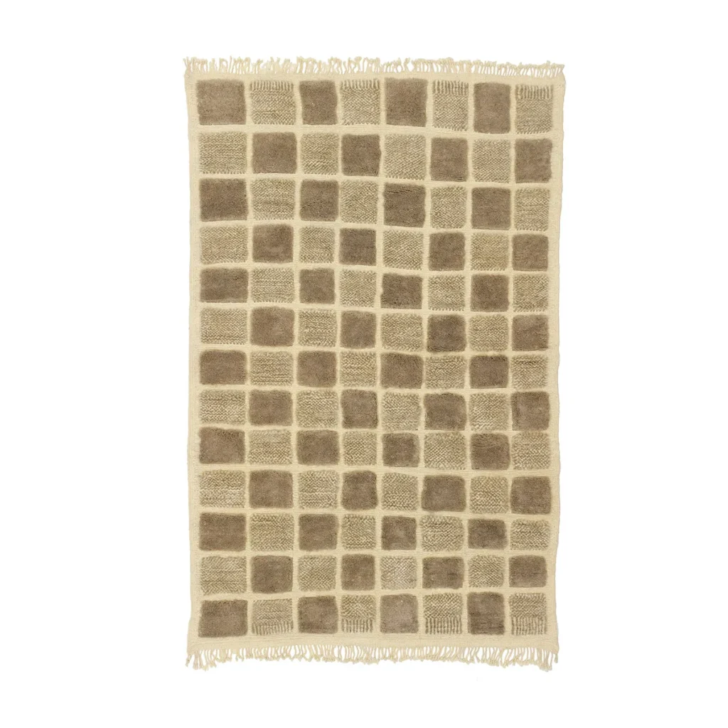 This luxury rug boasts a rectangular shape with a grid pattern of darker beige squares and fringed edges, showcasing exquisite craftsmanship.