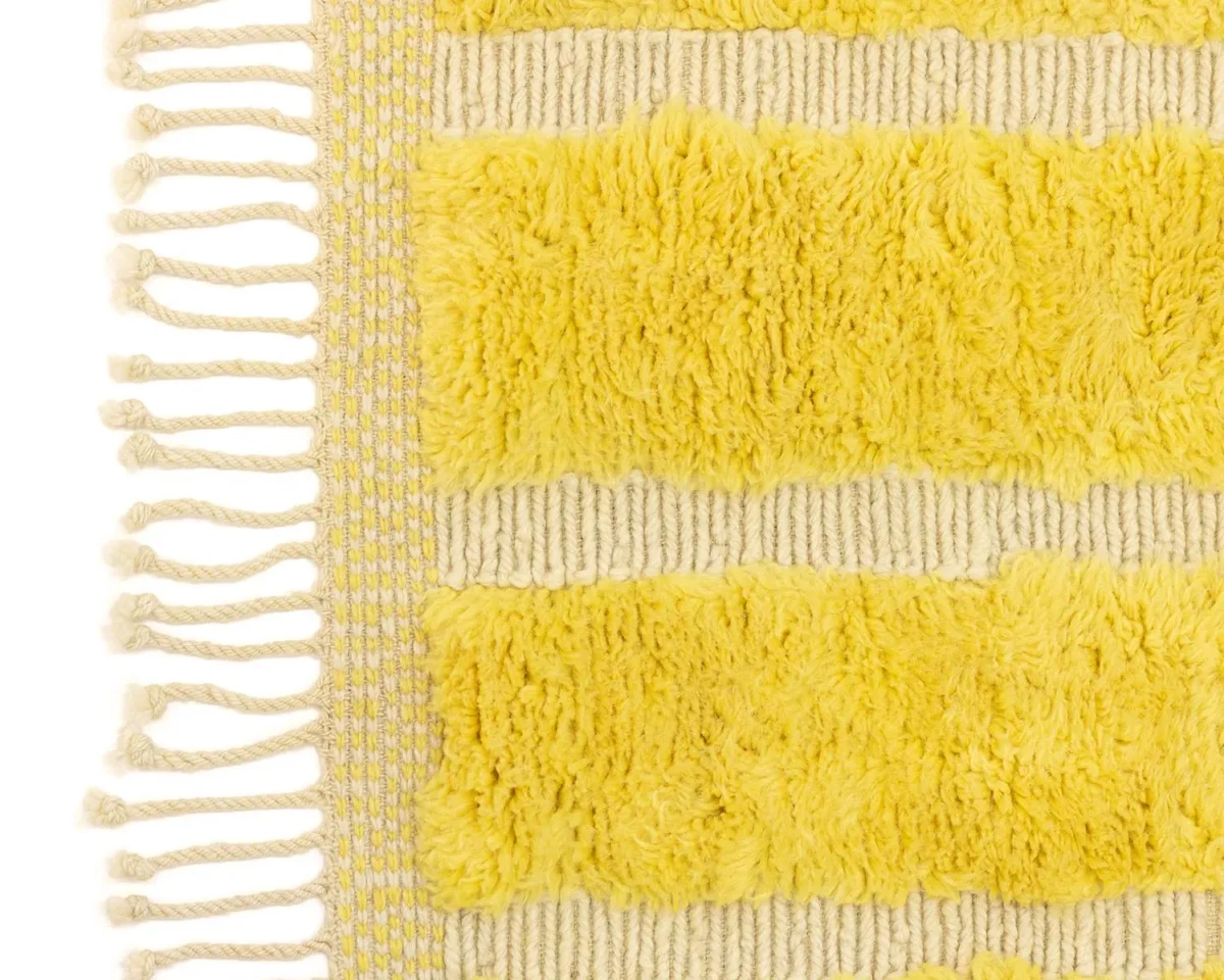 Experience the exquisite detail of this hand-knotted rug. The close-up reveals a textured yellow and beige design with fringed edges, showcasing alternating fluffy and flat horizontal stripes. Perfect as a luxurious addition to elevate your living space.