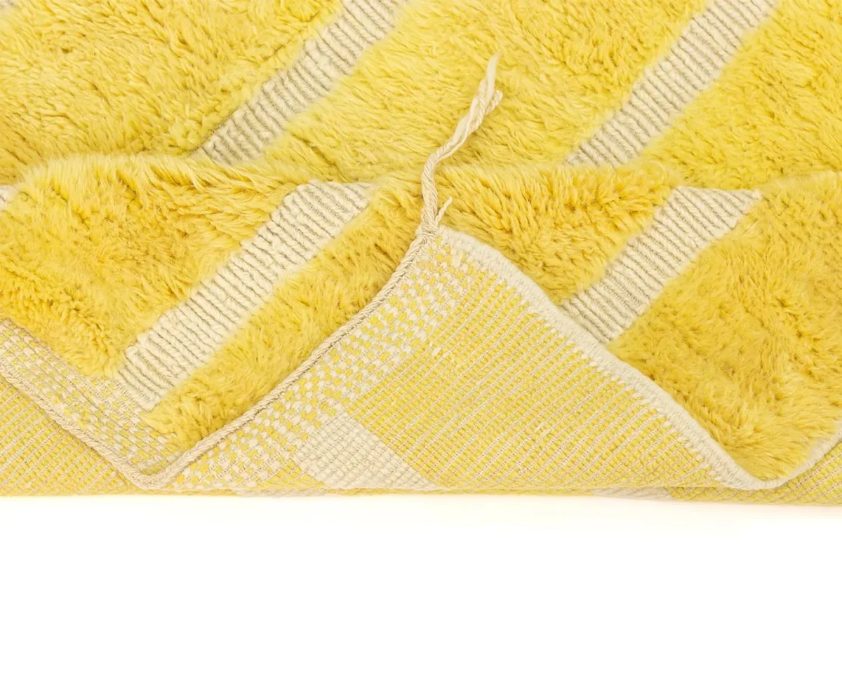 Close-up of a luxurious yellow patterned rug with a corner flipped over, revealing its intricately woven underside.