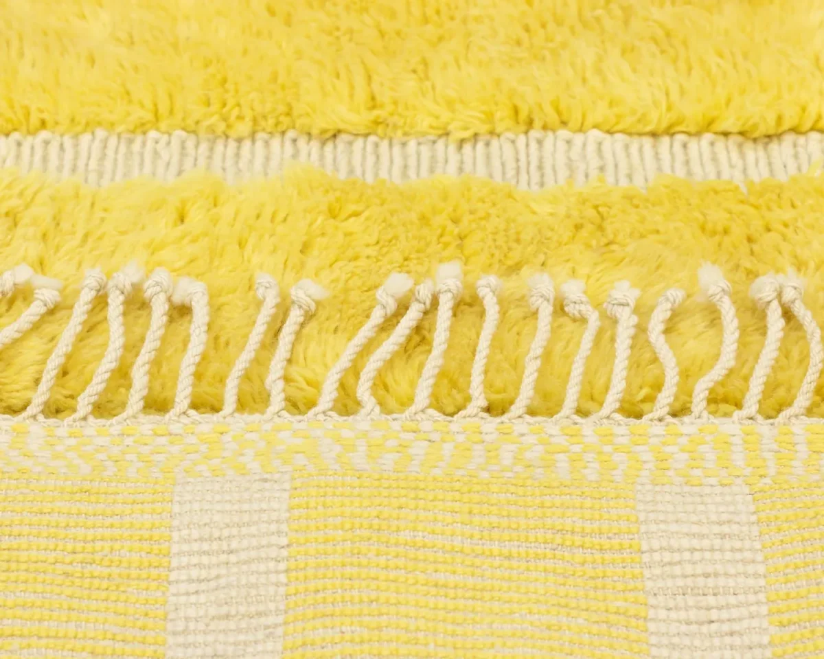 Close-up of a textured yellow and white woven textile with fringe detailing, showcasing the elegance of hand-knotted rugs.