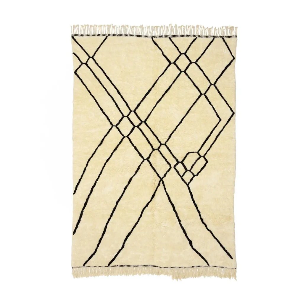 This hand-knotted rectangular beige rug features a striking black geometric line pattern and fringed edges, reminiscent of authentic Moroccan rugs.