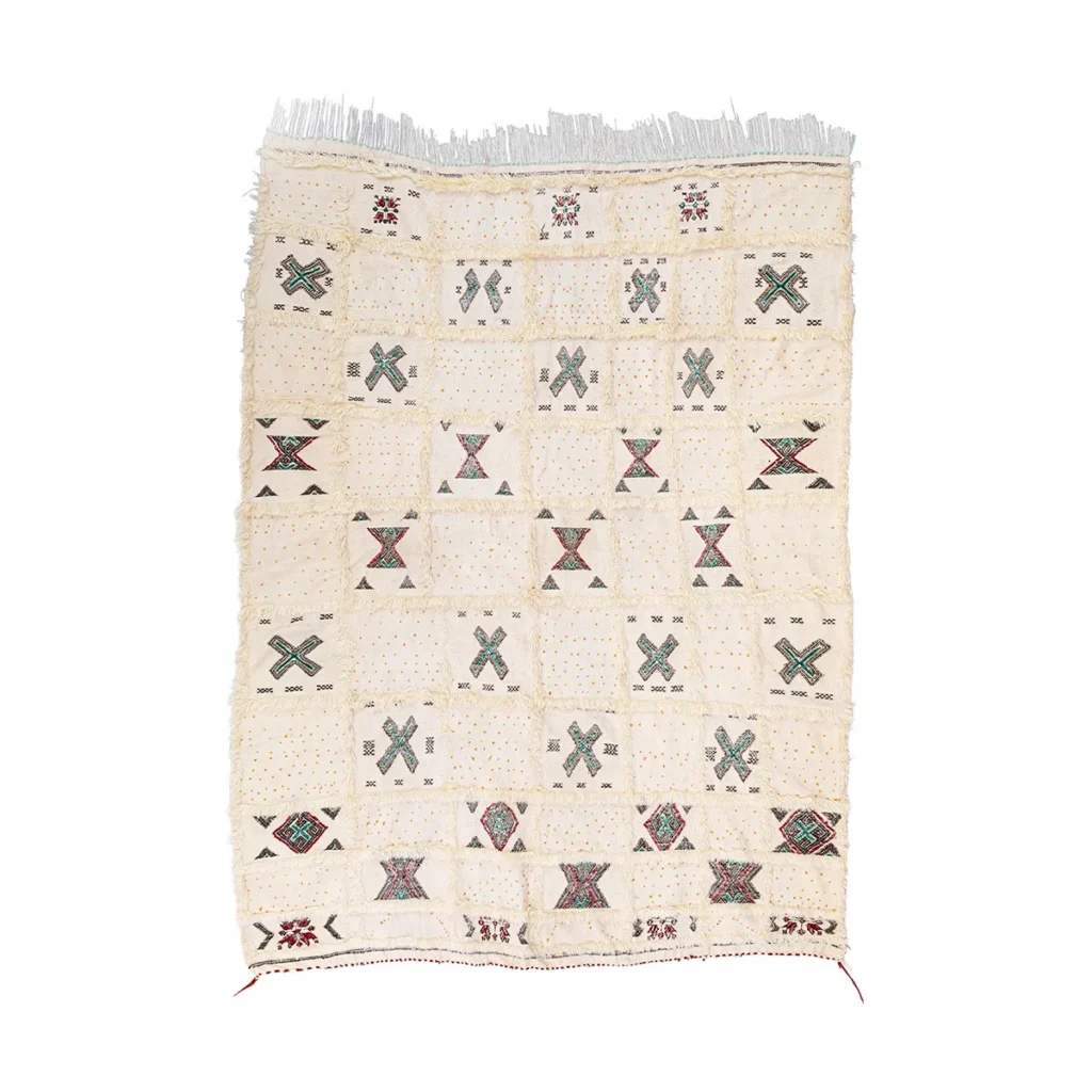This rectangular, cream-colored textile is a hand-knotted rug that showcases a geometric pattern with fringed edges. The design exhibits multicolored, symmetrical shapes evenly spaced across the fabric, adding an element of luxury to any space.