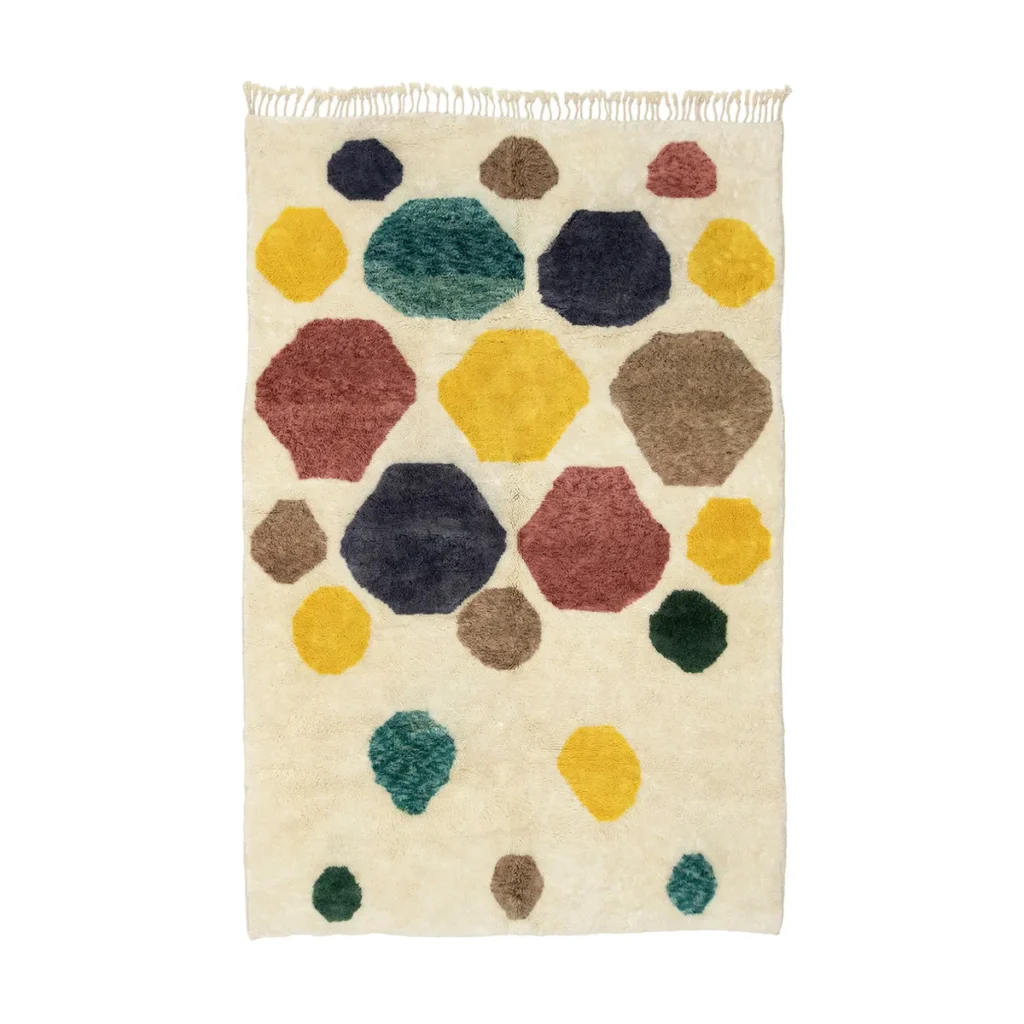 This hand-knotted rug boasts a cream background adorned with vibrant hexagonal shapes in yellow, red, green, and blue. As part of the luxury home decor collection, it is elegantly finished with tassels along the top edge.