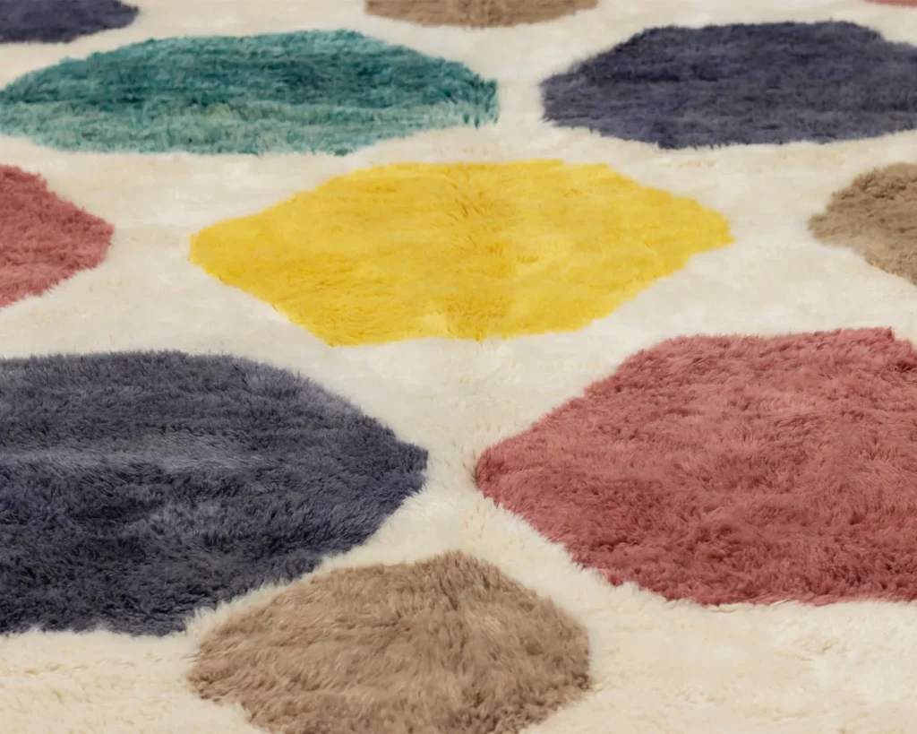 A close-up of a luxury rug showcases intricate hexagonal shapes in vibrant colors like yellow, blue, green, red, and brown against a light background. This hand-knotted masterpiece exemplifies the finest in handmade home decor.