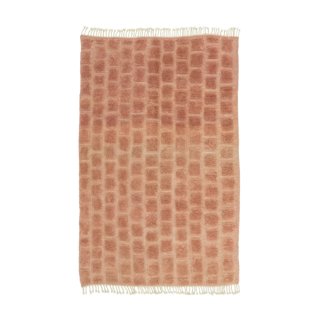 A luxurious rectangular pink and beige rug displays a tiled pattern with fringed edges, exemplifying exquisite craftsmanship. This handmade home decor piece is a stunning addition to any room, offering elegance and style.