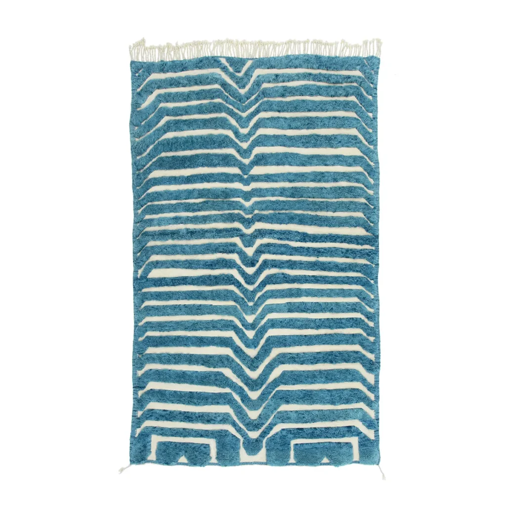 This handcrafted Moroccan rug features a blue and white striped design with an elegant zigzag pattern and fringe at the top, adding a touch of luxury to any space.