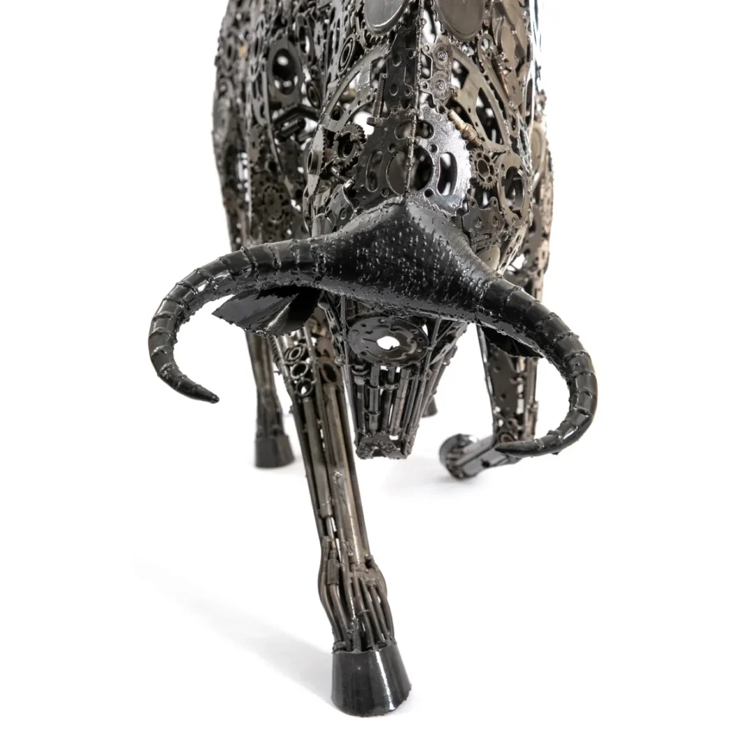 A dynamic recycled bull sculpture, made of interlocking metal parts, showcases detailed horns and a bold forward motion stance, embodying the artistry of metalwork.