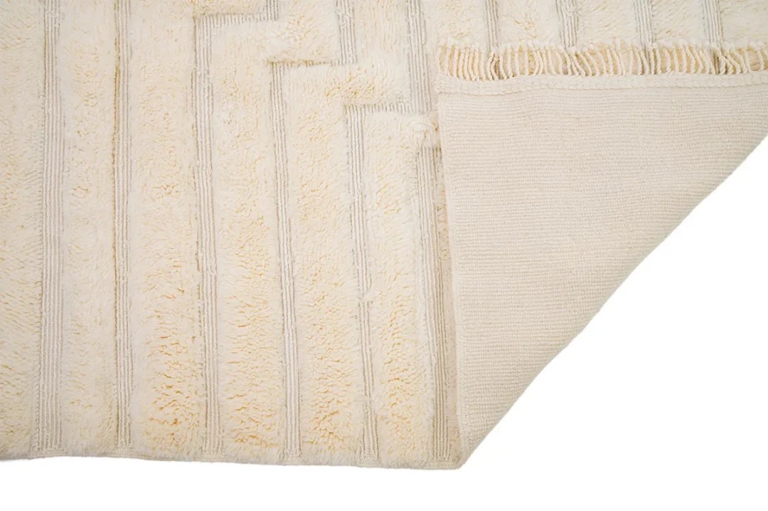 Beige rug with raised striped texture and fringe on one side. Bottom corner flipped over to show underside.