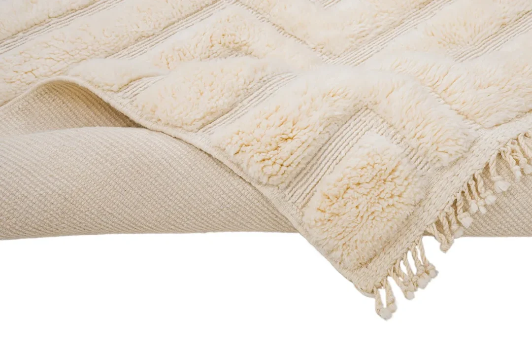 A cream-colored woven blanket with textured patterns and fringe edges is folded.