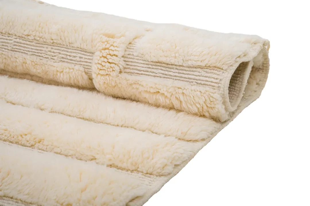 A beige, rolled-up, fluffy area rug shown with horizontal ridged patterns and a soft texture.