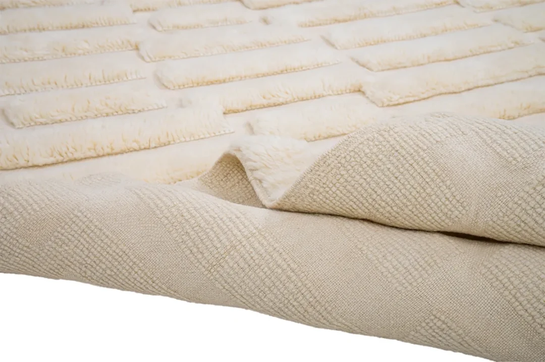 A cream-colored textured blanket with a patterned design is folded over, showing both sides.