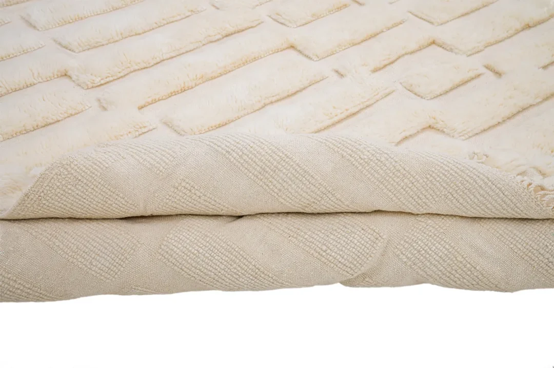 A folded beige textured blanket with a diamond and square woven pattern.