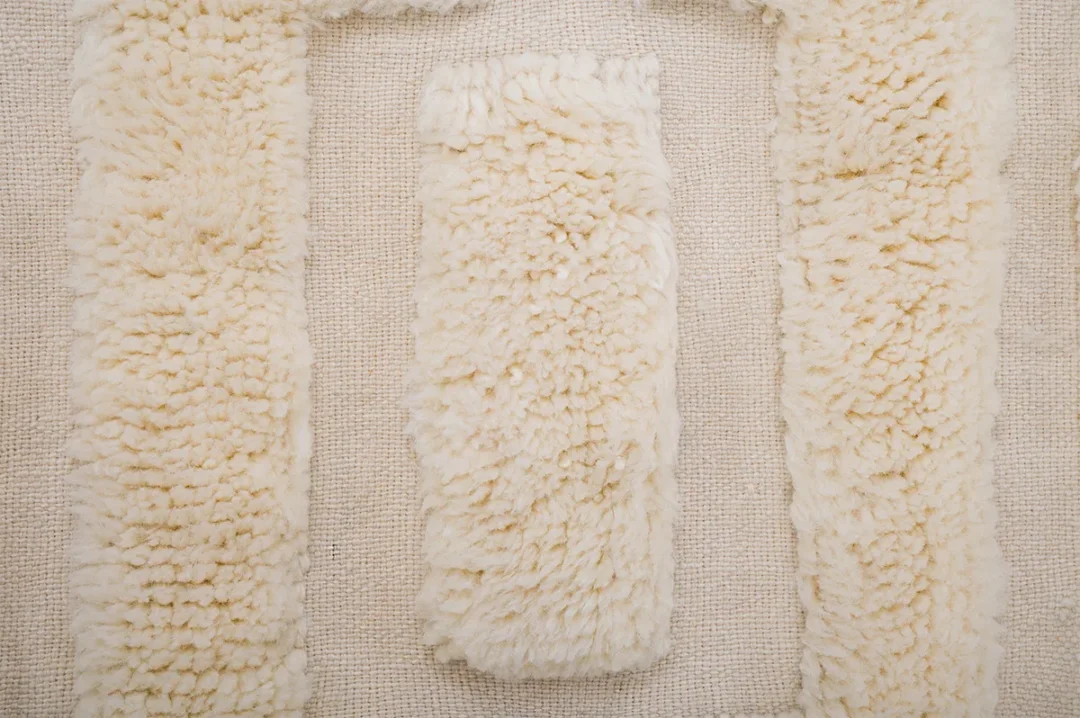 A textured beige surface with three rectangular sections of thick, fluffy material arranged in an inverted U shape against a woven background.