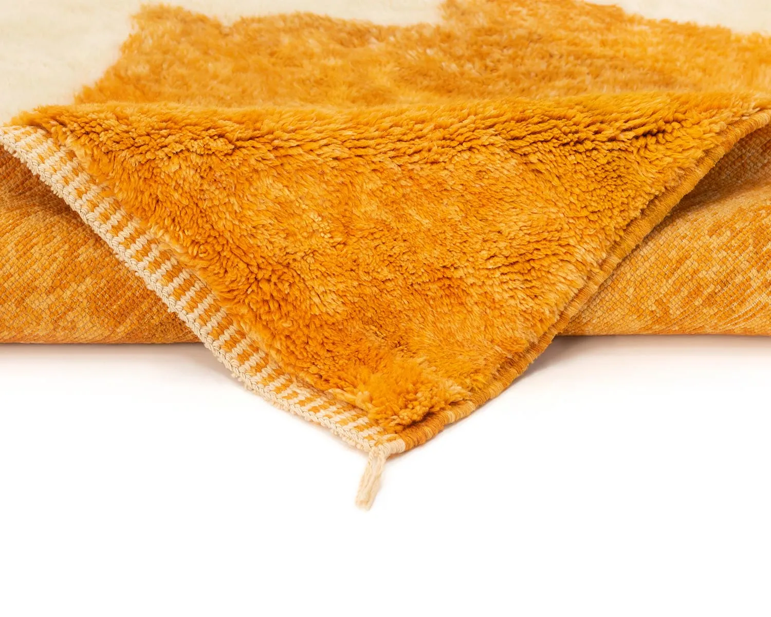 Close-up of a folded orange and beige plush rug, showing a fluffy texture and a stitched edge detail.