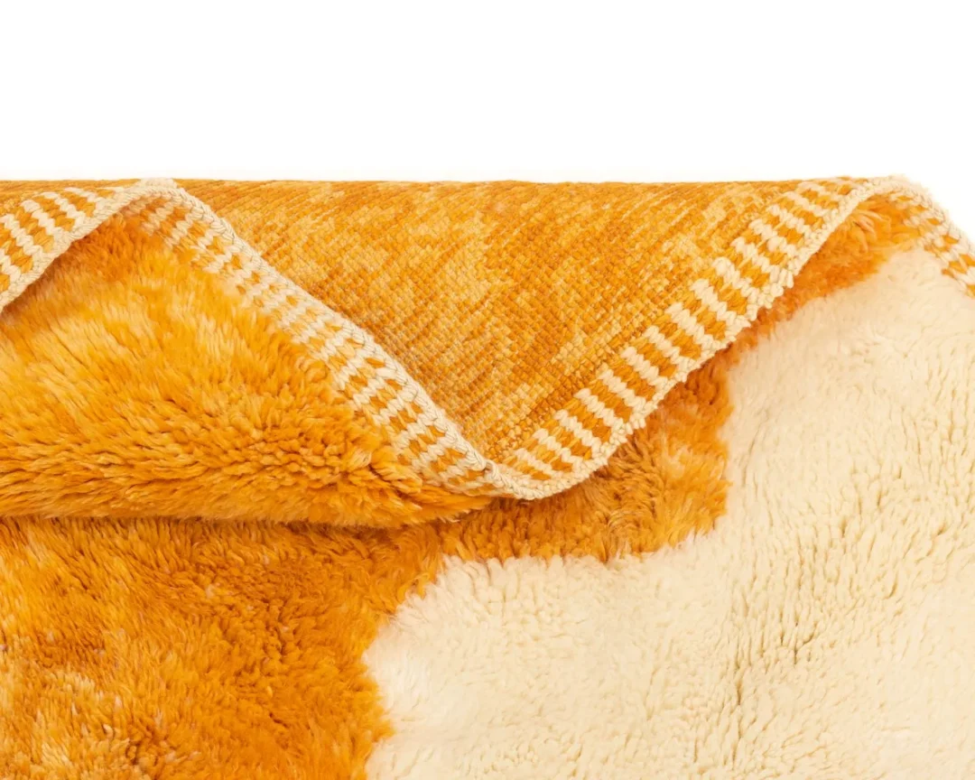 Close-up of a folded, fluffy orange and cream blanket with a striped trim along the edge.