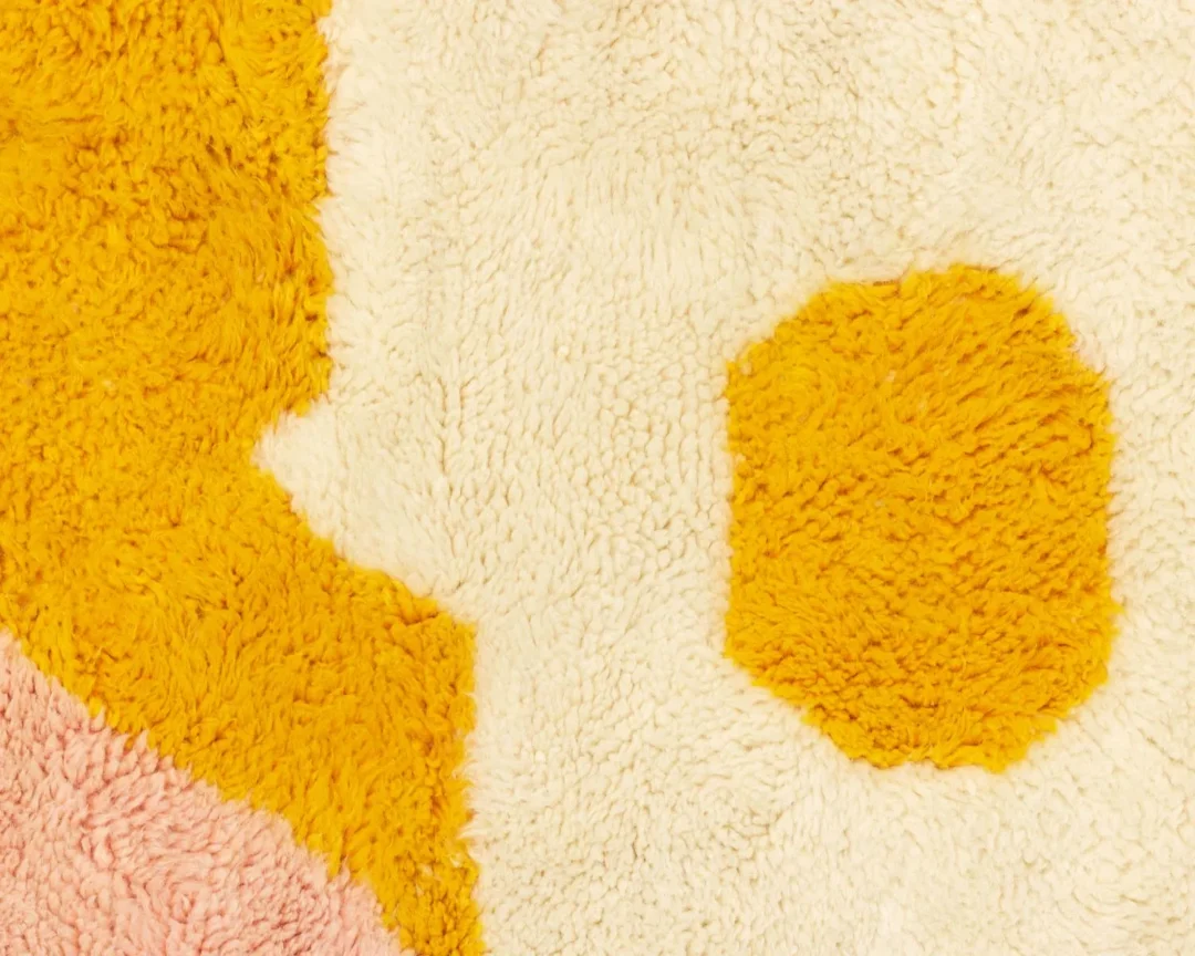 Close-up of a textured, fluffy rug with cream, pink, and yellow patterns in irregular shapes.