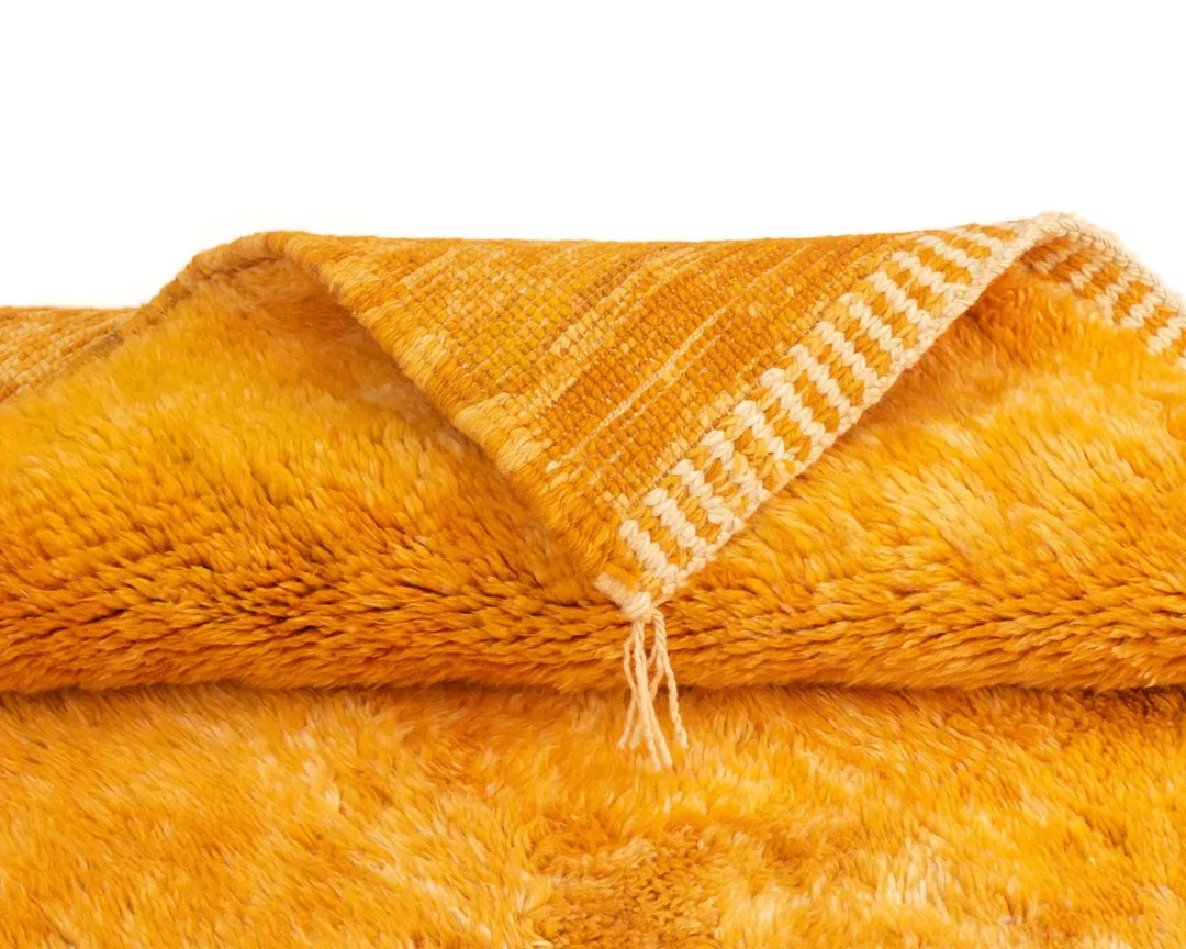 Close-up of a folded, soft orange fabric with a fuzzy texture and a contrasting woven edge.