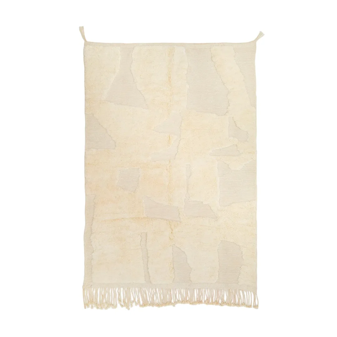 A beige textured wall tapestry with abstract patterns and fringe at the bottom.