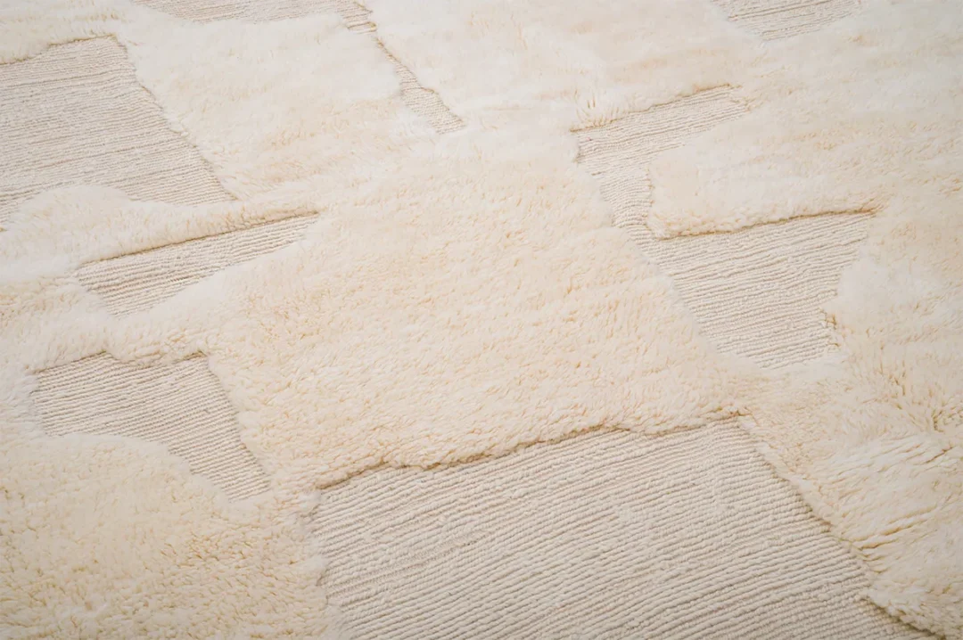 Close-up of a beige textured rug with a combination of plush and woven sections, creating a patchwork pattern.