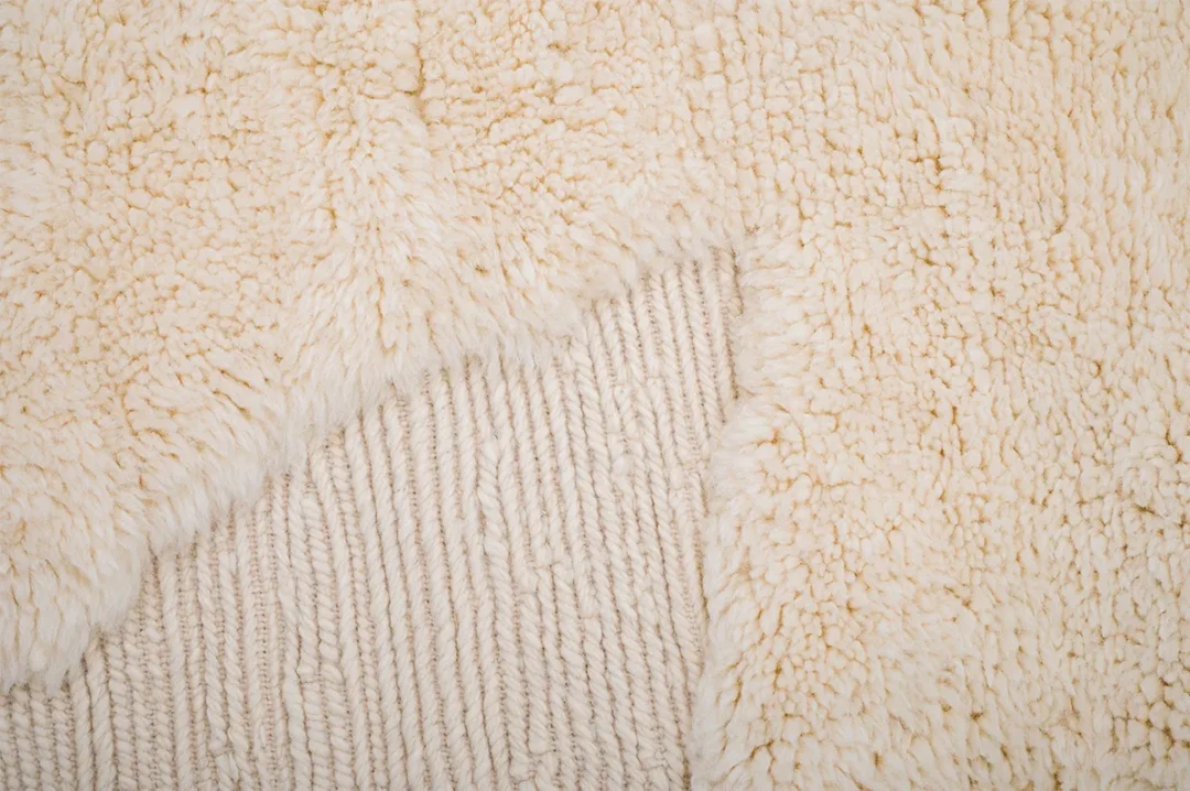 Close-up of a beige textured fabric with a fluffy fleece overlay and a ribbed base layer visible at the corner.