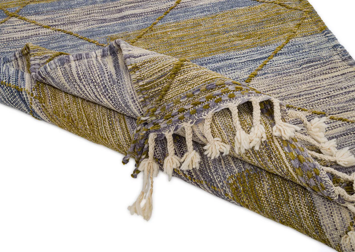 A woven rug with geometric patterns in green, blue, and white, featuring tassels on one edge, is partially folded over.