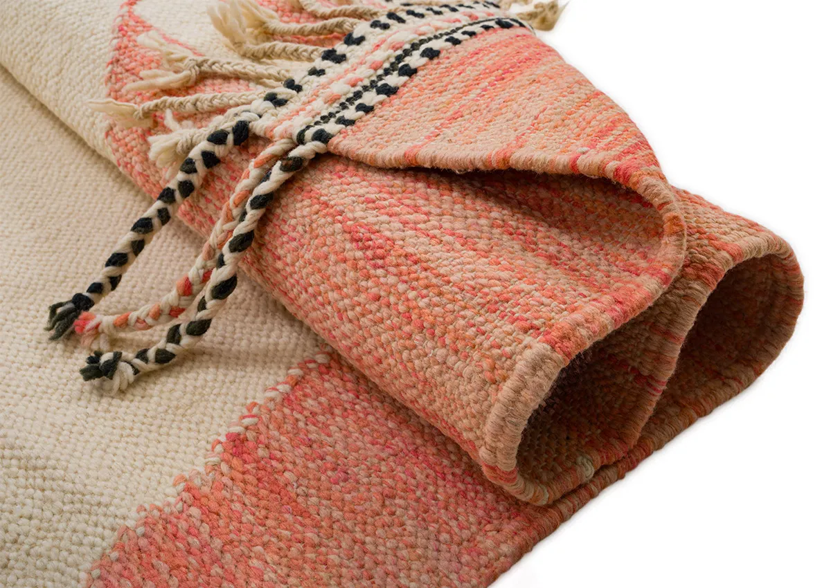 A rolled-up woven blanket with a cream and pink pattern and decorative tassels.