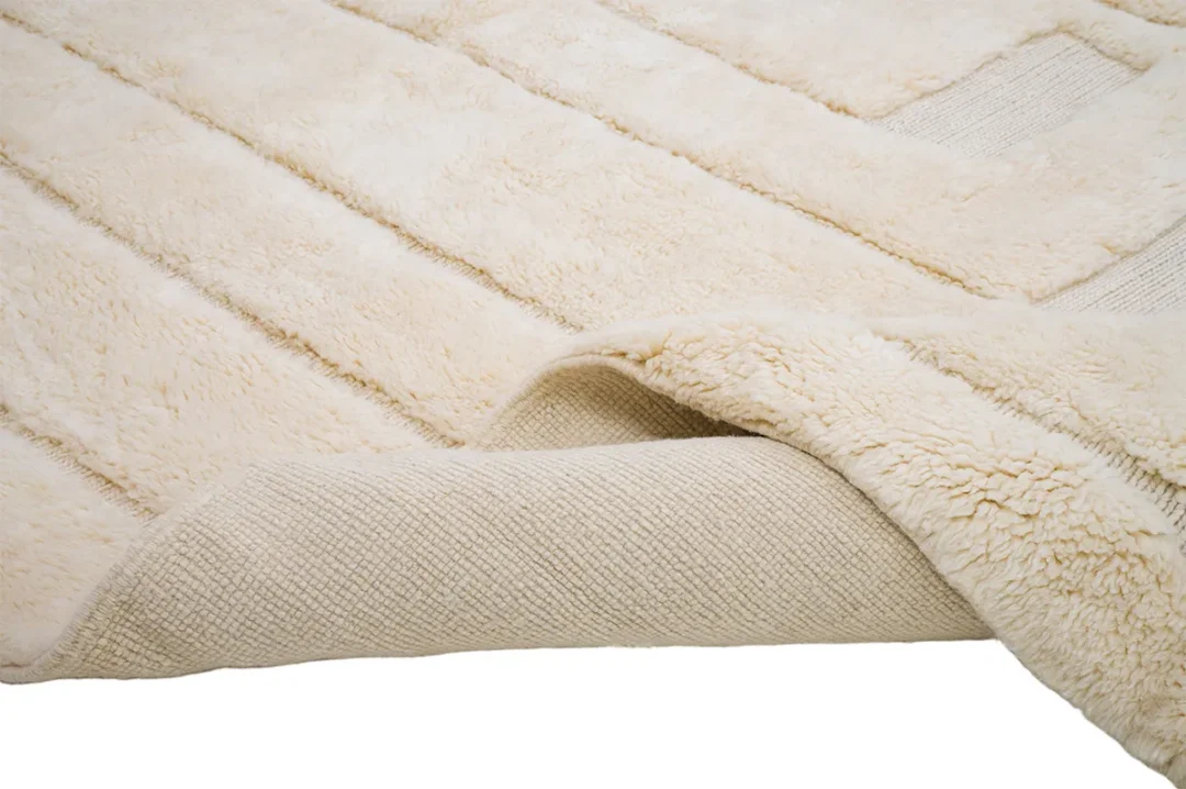 A beige fluffy rug with a textured underside partially folded over, displayed on a white background.