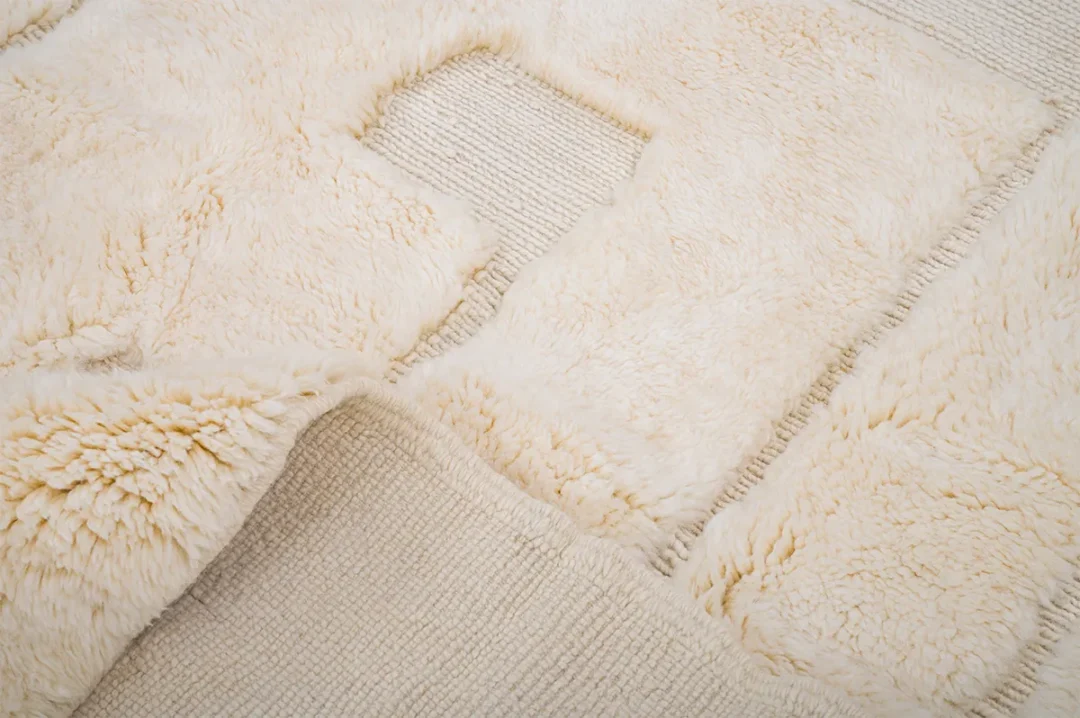 Close-up of a textured beige and cream rug with a mix of plush and woven patterns, featuring a rectangular cutout design.