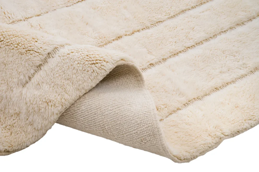 Close-up of a beige, fluffy rug with folded corner, showing its textured underside.