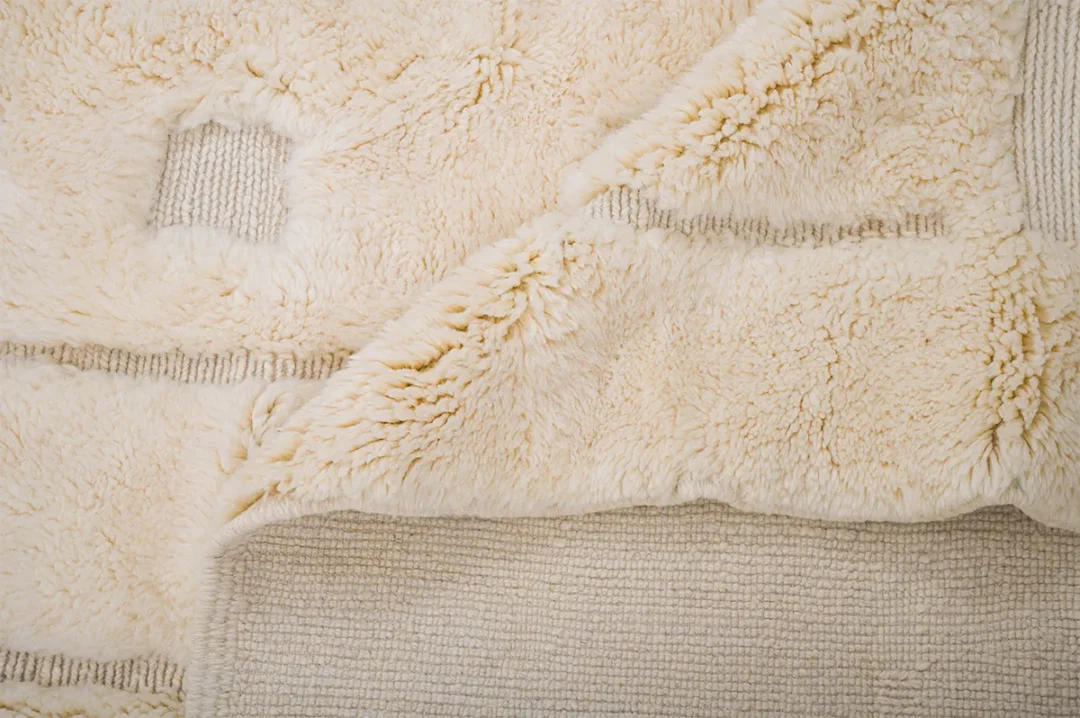 A beige, fluffy fabric with a grid pattern is partially folded, revealing a smoother texture on the back.