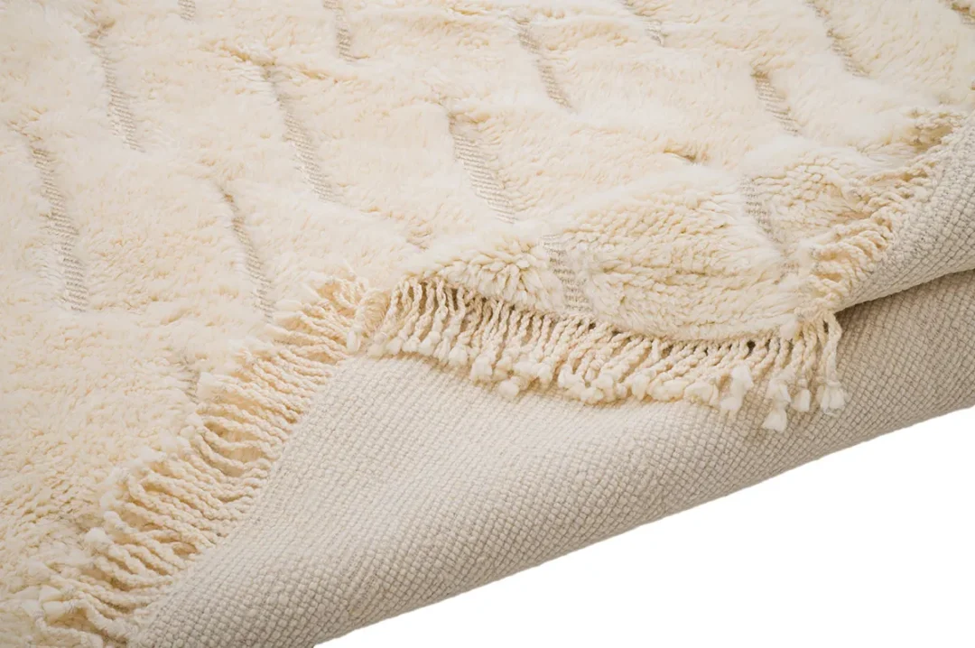 Close-up of a cream-colored textured rug with tassels on the edge, displaying a woven pattern.