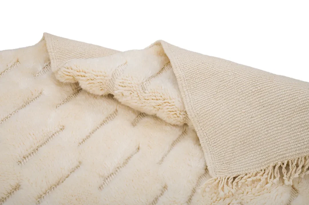 A beige fringed throw blanket, featuring a soft, textured fur-like surface with a striped pattern, partially folded.