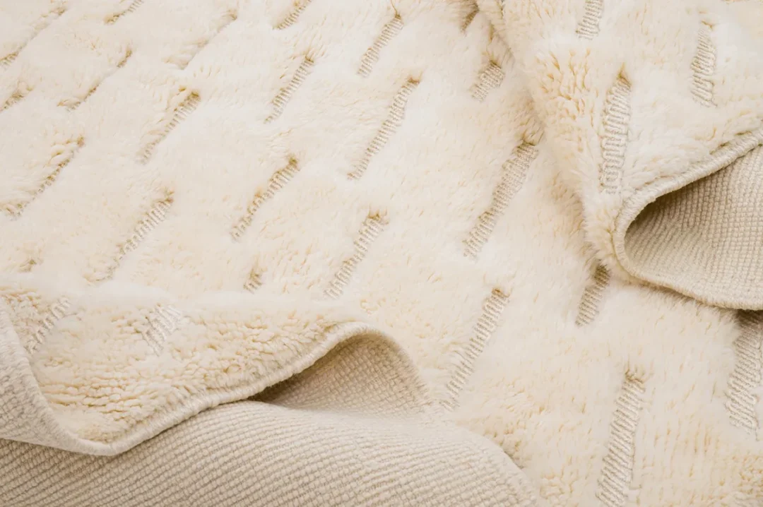 Close-up of a beige textured fabric with a pattern of parallel lines. The fabric appears soft and plush, showing folds and varying textures.