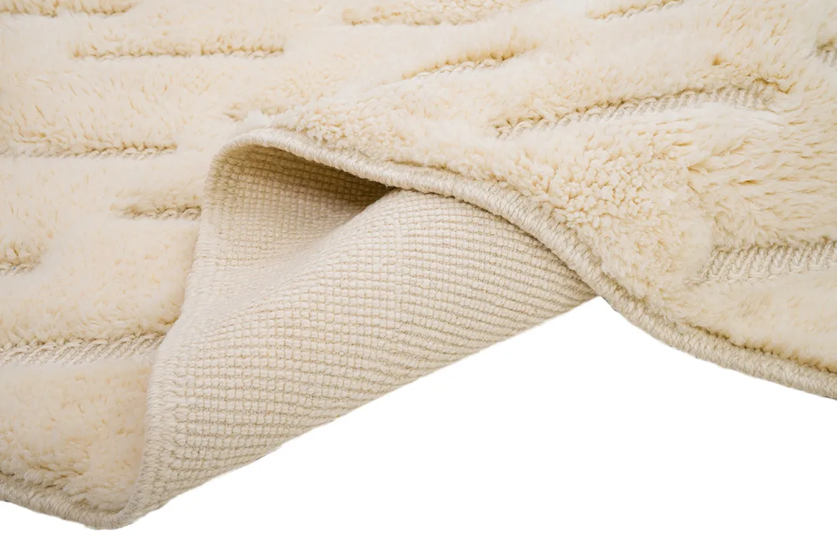 Cream-colored textured rug with thick, plush fibers partially rolled to reveal a woven underside.