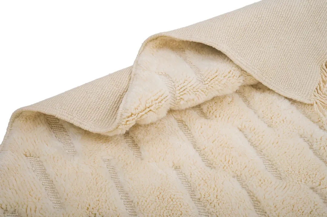 A plush beige rug partially folded to show both the textured surface and pile, displaying its soft, fluffy texture and woven underside.